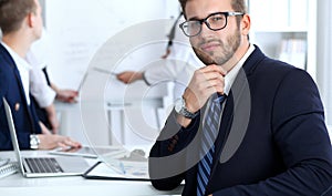 Business people at meeting in office. Focus at cheerful smiling bearded man wearing glasses. Conference, corporate