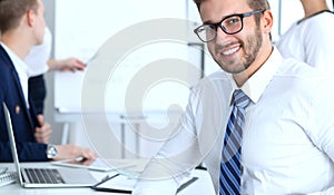 Business people at meeting in office. Focus at cheerful smiling bearded man wearing glasses. Conference, corporate