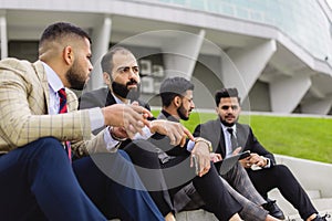 Business people outdoor meeting. A company of male businessmen in suits are sitting on the steps of the stairs. Working