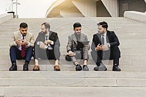 Business people outdoor meeting. A company of male businessmen in suits are sitting on the steps of the stairs. Working