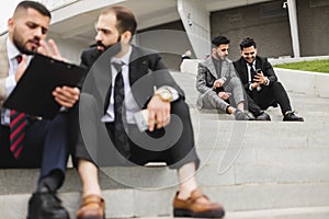 Business people outdoor meeting. A company of male businessmen in suits are sitting on the steps of the stairs. Working