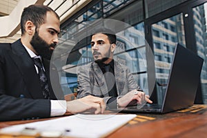 Business people outdoor meeting. A group of business people meet outdoors. Two men are using a laptop. Working break