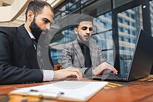 Business people outdoor meeting. A group of business people meet outdoors. Two men are using a laptop. Working break