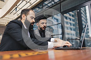 Business people outdoor meeting. A group of business people meet outdoors. Two men are using a laptop. Working break