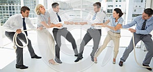 Business people playing tug of war in office