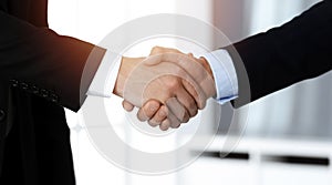 Business people shaking hands after contract signing while standing in sunny office. Teamwork and handshake concept