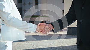 Business people shaking hands. Handshake between business man and business woman outdoors by business office building.