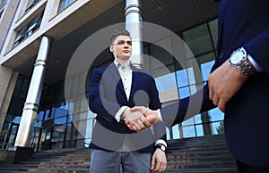 Business people shaking hands outside modern office building.