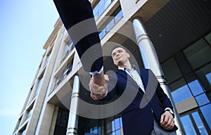 Business people shaking hands outside modern office building.