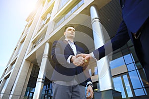 Business people shaking hands outside modern office building.