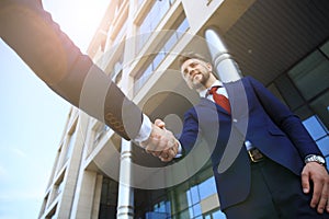 Business people shaking hands outside modern office building.