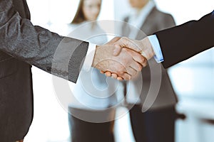 Business people shaking hands while standing with colleagues after meeting or negotiation, close-up. Group of unknown