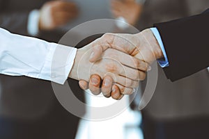 Business people shaking hands while standing with colleagues after meeting or negotiation, close-up. Group of unknown