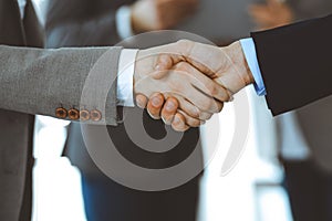 Business people shaking hands while standing with colleagues after meeting or negotiation, close-up. Group of unknown