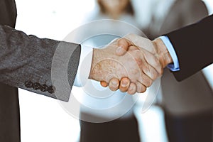 Business people shaking hands while standing with colleagues after meeting or negotiation, close-up. Group of unknown