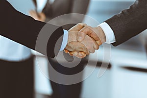 Business people shaking hands while standing with colleagues after meeting or negotiation, close-up. Group of unknown