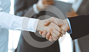 Business people shaking hands while standing with colleagues after meeting or negotiation, close-up. Group of unknown