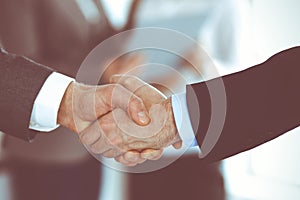 Business people shaking hands while standing with colleagues after meeting or negotiation, close-up. Group of unknown