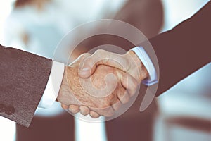 Business people shaking hands while standing with colleagues after meeting or negotiation, close-up. Group of unknown