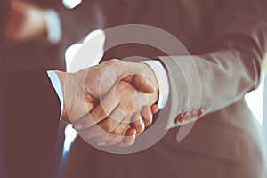 Business people shaking hands while standing with colleagues after meeting or negotiation, close-up. Group of unknown