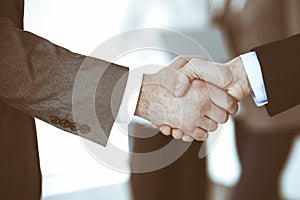 Business people shaking hands while standing with colleagues after meeting or negotiation, close-up. Group of unknown