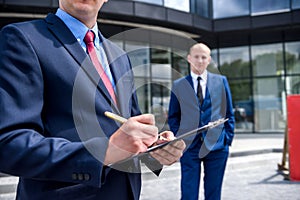 Business people signing contract near skyscraper outdoors