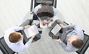 Business people sit on chairs with tablet and commercial business charts and discuss work plans top view