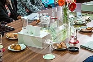 Business people sitting on a table for conference with cookies glass and jar of water placed on wooden table