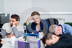 Business people sleeping in the conference room during a meeting, while their colleague is trying to concentrate on the