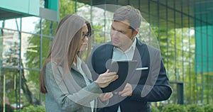 Business people standing near business center with digital tablet. Man and woman read news on Tablet Computer near