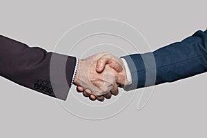 Business people in suit shaking hands, success in business concept, on grey studio wall background