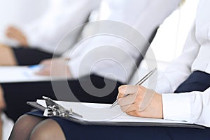 Business people taking part at conference or training at office, close-up. Women sitting on chairs and making notes like