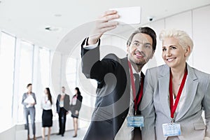 Business people taking selfie in convention center with colleagues walking in background