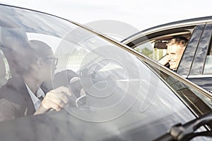 Business people talking while sitting in cars against sky