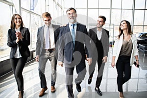 Business People Team Walking In Modern Office, Confident Businessmen And Businesswomen With Mature Leader In Foreground.