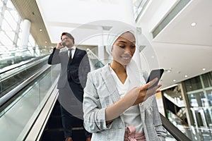 Business people using mobile phone on escalator in a modern office