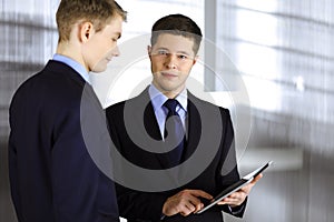 Business people are using a tablet computer, while standing in a modern office. Unknown businessman with a colleague at