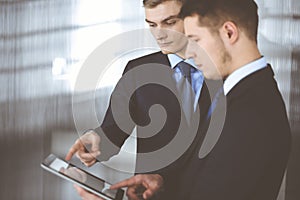 Business people, using a tablet computer, while standing in a modern office. Unknown businessman with a colleague at