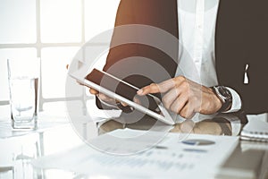 Business people using tablet computer while working together in sunny office. Unknown businessman sitting at the desk