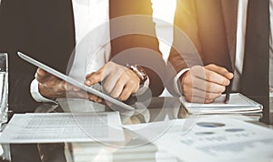 Business people using tablet computer while working together in sunny office. Unknown businessman sitting at the desk