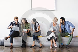 Business people using technologies while sitting against wall