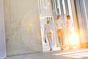 Business people walking while talking in office corridor with yellow lens flare in background