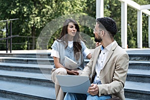 Business people working outside on laptop and tablet sitting on the stairs in front of office building. Colleagues businessman and