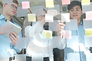 Business people working planning discussing idea with sticky reminder note on glass wall