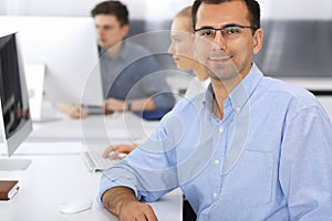 Business people working together in modern office. Focus at happy smiling adult businessman or entrepreneur using pc