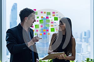 Business people working and use paper notes to share idea on the glass window in office. Businessman and Businesswoman work on