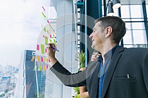 Business people working and use post it notes to share idea on the glass window in office. Businessman and Businesswoman work on