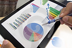 Business person analyzing financial statistics displayed on the tablet screen with a pen