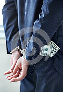 Business person, hands and cash with handcuffs for bribe, secret or corruption in financial crime. Closeup or rear view