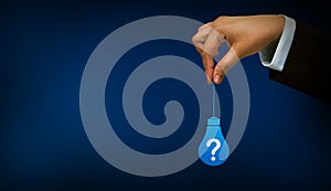 Business person holding bulb with question mark sign	on blue background